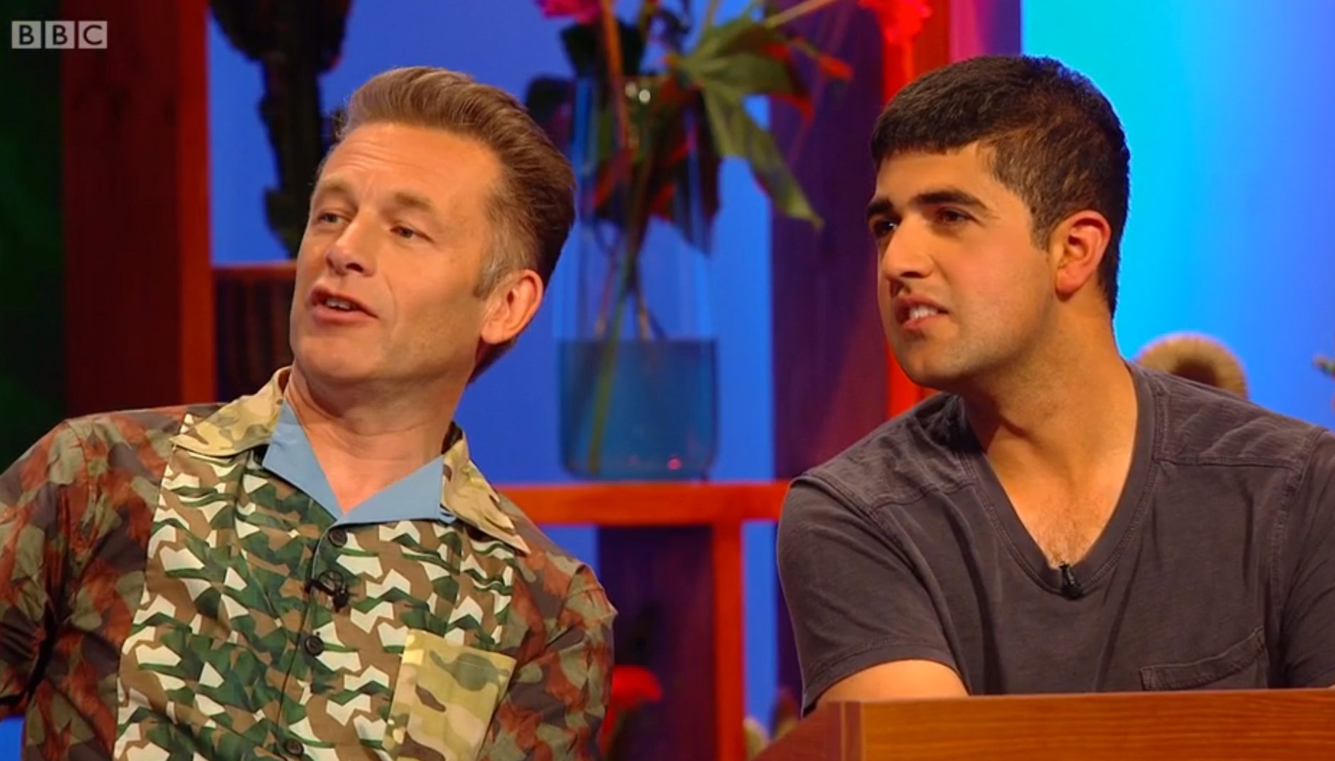 Ajay Tegala and Chris Packham Chris and Ajay sat in a studio, Chris is wearing a colourful green and brown shirt and Ajay is wearing a blue T-shirt, they are wearing lapel microphones and are lit by the studio lights