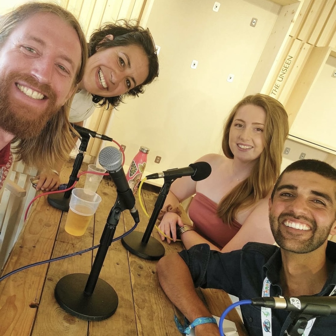VOICE Into the Wild Selfie of four smiling faces people sat around microphones: Left to right: Ryan (beard and long hair), Nadia (shortish dark hair), Ezz (long fair hair), Ajay (beard and very short dark hair)