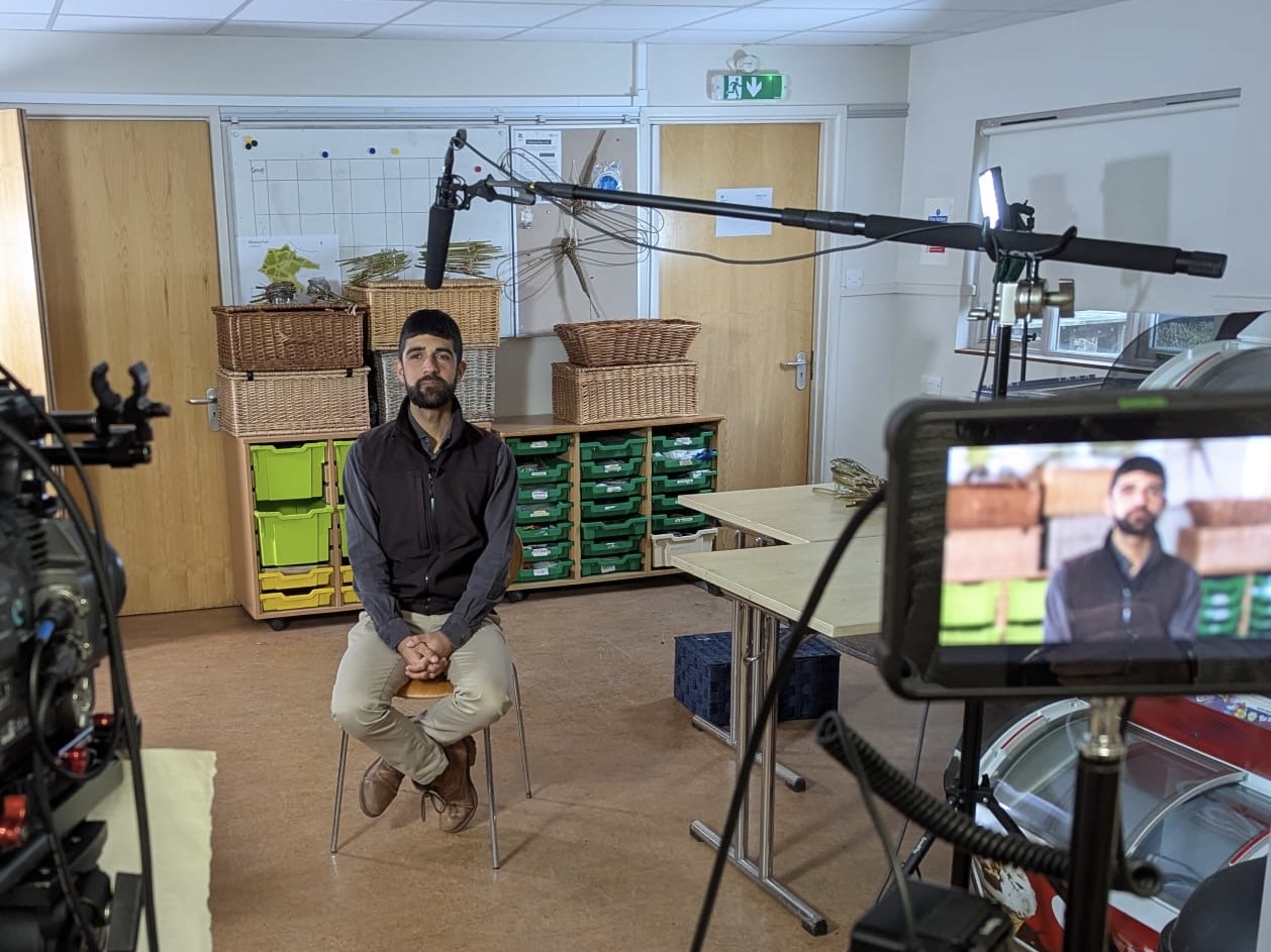 Ajay Tegala being filmed at Wicken Fen A man sat on a stool with two cameras in front of him