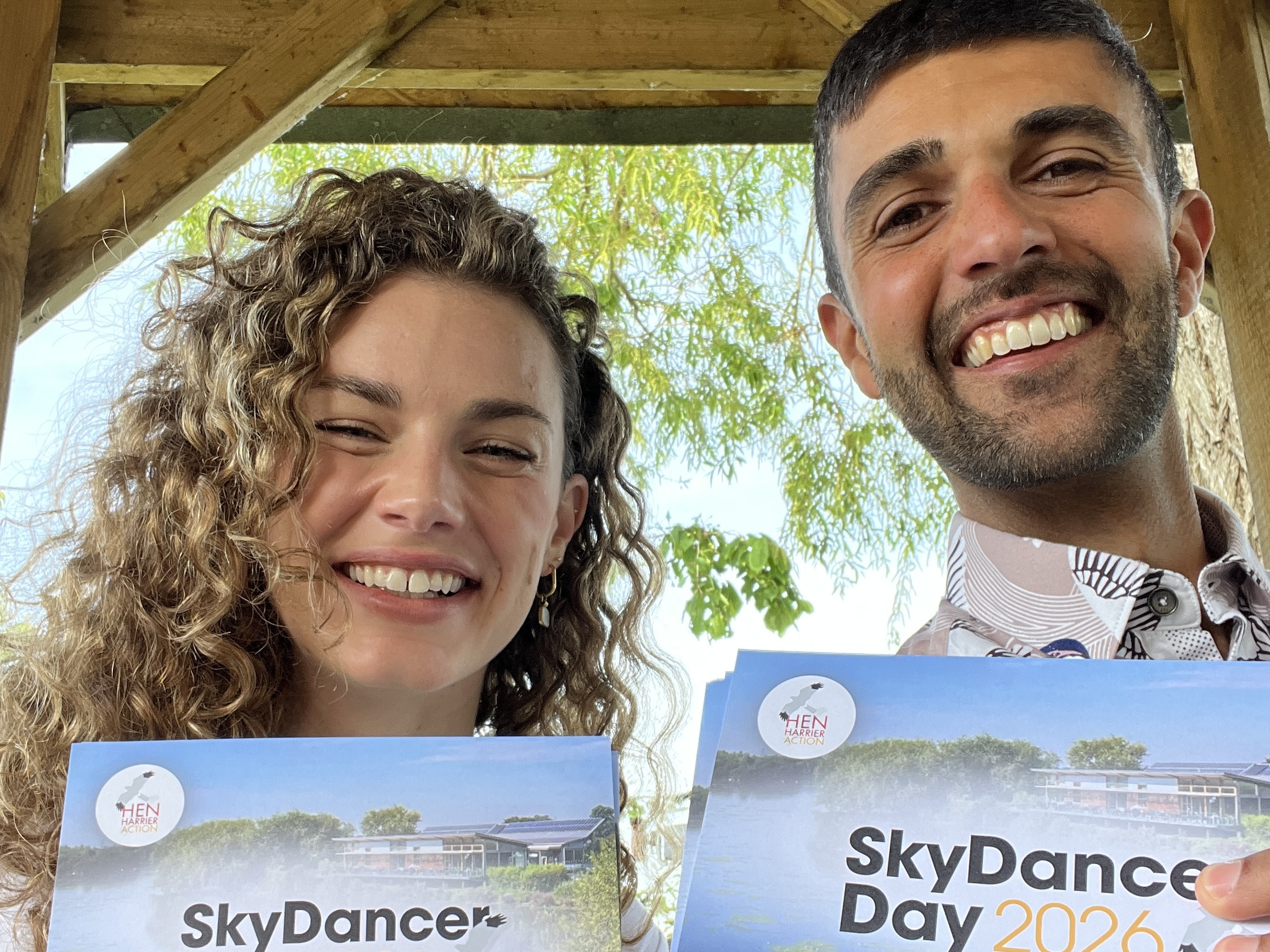 Ajay and Lauren present SkyDancer Day for Hen Harrier Action A smiling man and woman holding cue cards that say SkyDancer Day on them
