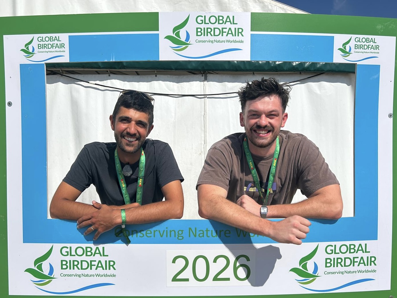 Ajay Tegala and Jake Brass at Global BirdFair Two men leaning on a sign that says Global BirdFair