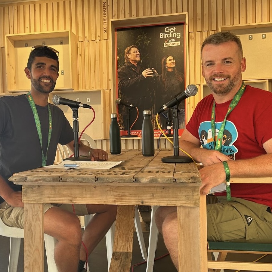 Two men sat on a stage, each with a microphone in front of them