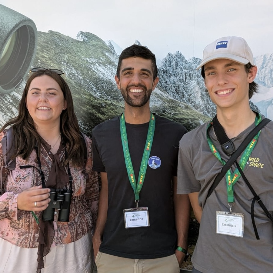 Three smiling young people in front of a poster of mountains