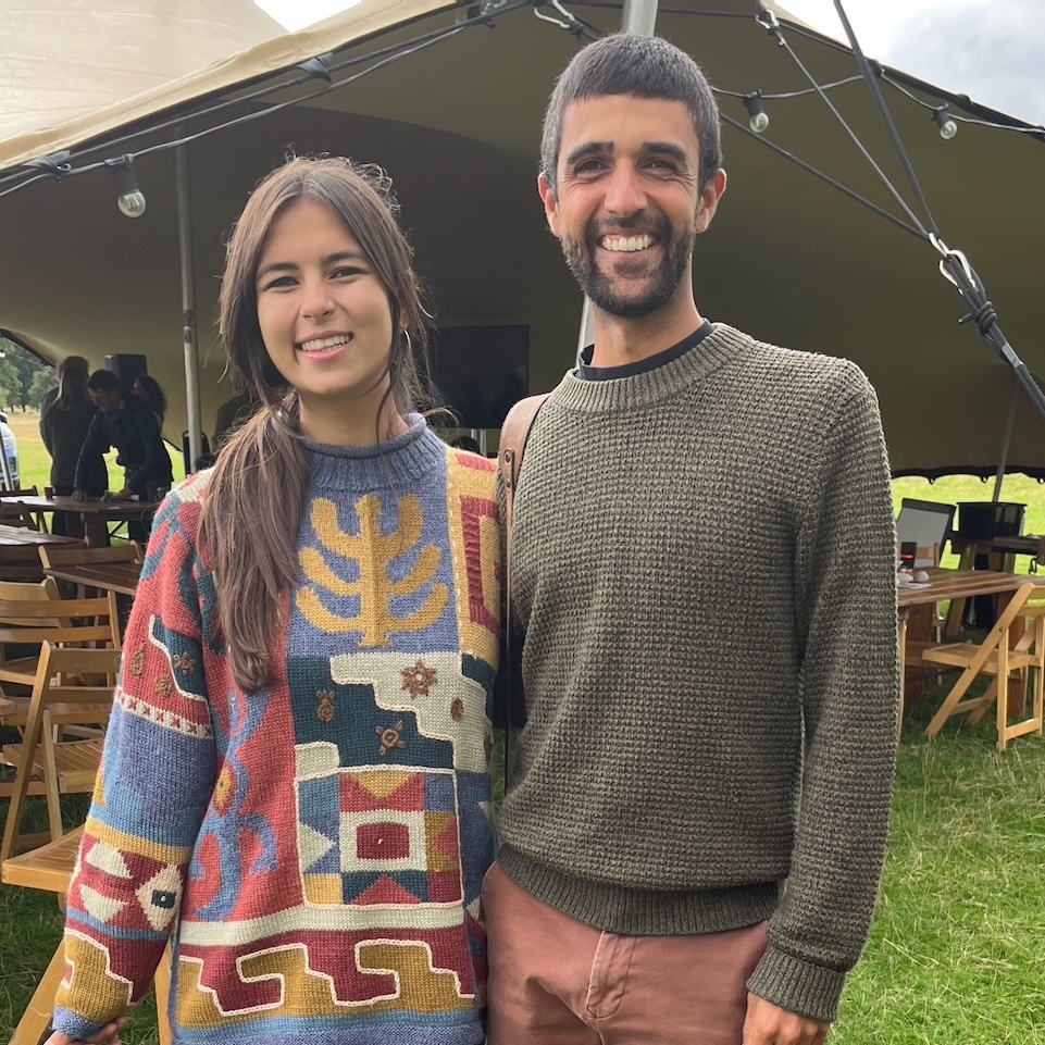 A young woman and young man stood smiling together in front of a stretch tent