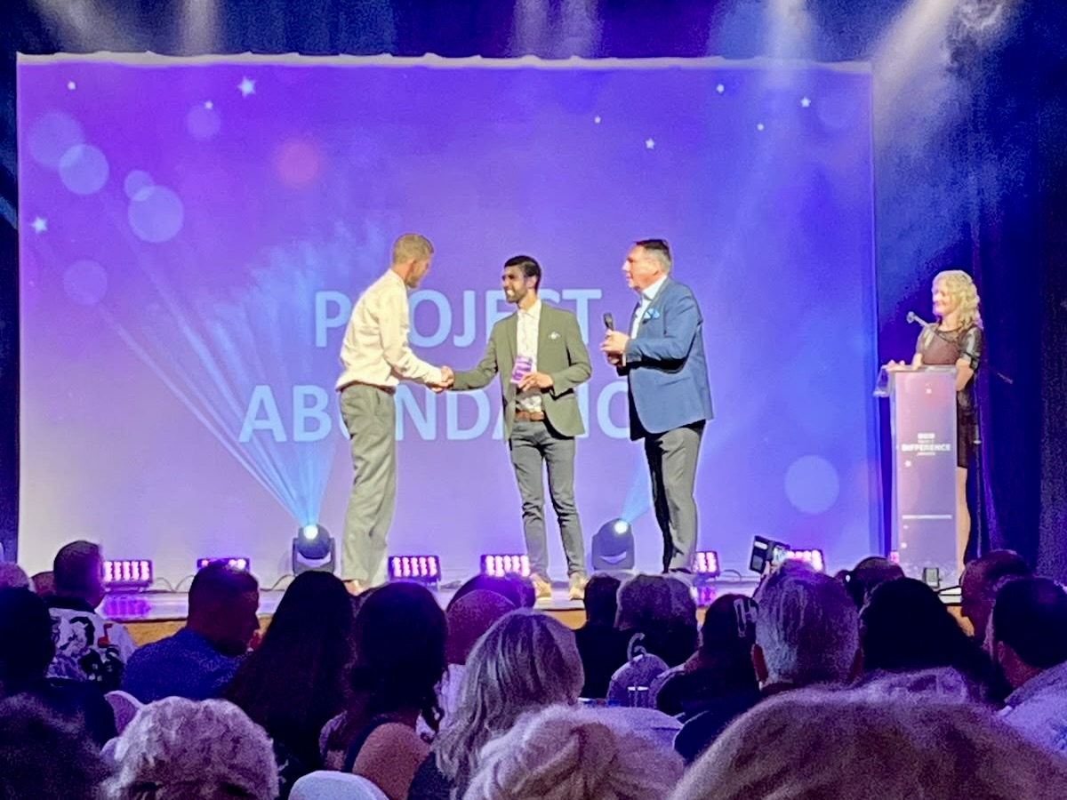 Ajay Tegala presents at the BBC Make A Difference Awards A man hands a trophy to another man on stage, with a big purple curtain behind